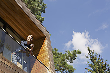 Germany, Berlin, Mature man standing on balcony and relaxing - SKF001092