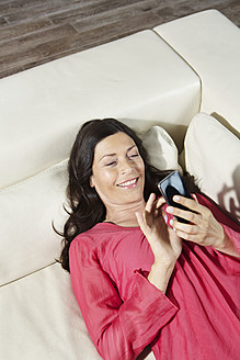 Deutschland, Berlin, Reife Frau liegt auf Sofa und benutzt Handy - SKF001122
