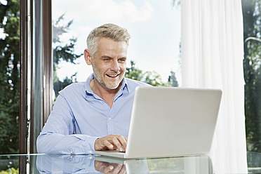 Deutschland, Berlin, Älterer Mann sitzt am Tisch und benutzt Laptop - SKF001144