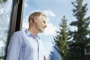 Deutschland, Berlin, Älterer Mann schaut durch Fenster, lächelnd - SKF001147