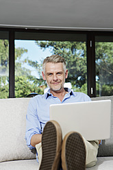 Germany, Berlin, Mature man using laptop, smiling, portrait - SKF001159