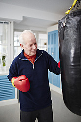 Germany, Duesseldorf, Senior man with boxing glove and punch bag - STKF000089