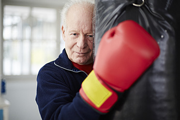 Germany, Duesseldorf, Senior man with boxing glove and punch bag - STKF000092