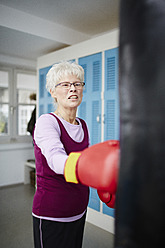 Germany, Duesseldorf, Senior woman with boxing glove and punch bag - STKF000093