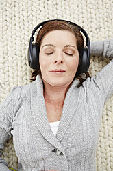 Germany, Duesseldorf, Mature woman lying on carpet and listening music - STKF000177