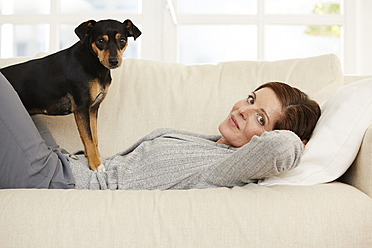 Deutschland, Düsseldorf, Reife Frau auf Sofa liegend mit Hund - STKF000195