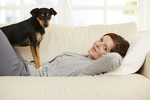 Germany, Duesseldorf, Mature woman lying on sofa with dog - STKF000195