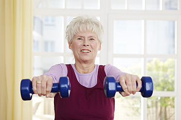 Germany, Duesseldorf, Senior woman exercising with barbell, smiling - STKF000182