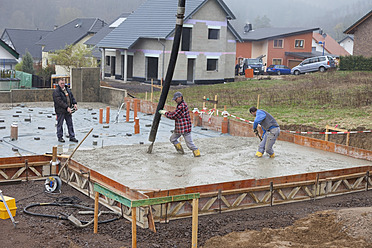 Europa, Deutschland, Rheinland-Pfalz, Bauarbeiter beim Einfüllen von Beton für das Fundament und Mann mit Fernbedienung - CSF016006