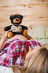 USA, Texas, Pregnant young woman holding teddy bear on belly - ABAF000493