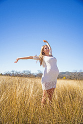 USA, Texas, Pregnant young woman stretching arms, smiling - ABAF000521