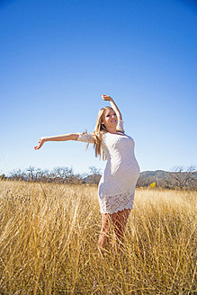 USA, Texas, Pregnant young woman stretching arms, smiling - ABAF000521