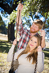 USA, Texas, Pregnant wife swinging while husband standing behind - ABAF000528
