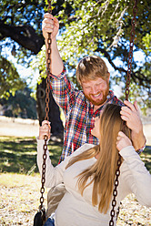 USA, Texas, Pregnant wife swinging while husband standing behind - ABAF000529