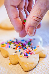 Human hand sprinkling rainbow icing over cookies - ABAF000571