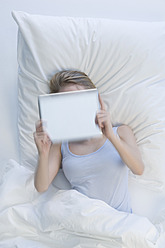 Germany, Young woman using digital tablet while lying on bed - CRF002235