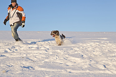 Deutschland, Bayern, Englischer Springer Spaniel und Hundehalter spielen im Schnee - MAEF005444