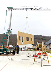 Europa, Deutschland, Rheinland-Pfalz, Männer, die einen Kran befestigen, schwenken die Wand eines Fertighauses über das Fundament - CSF016027