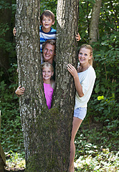 Austria, Portrait of friends standing behind tree trunk, smiling - WWF002734