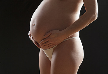 Schwangere Frau berührt ihren Bauch vor schwarzem Hintergrund - WWF002453