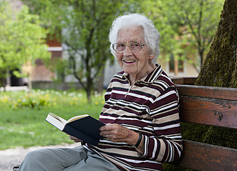 Österreich, Ältere Frau sitzt auf einer Bank und liest ein Buch - WWF002460