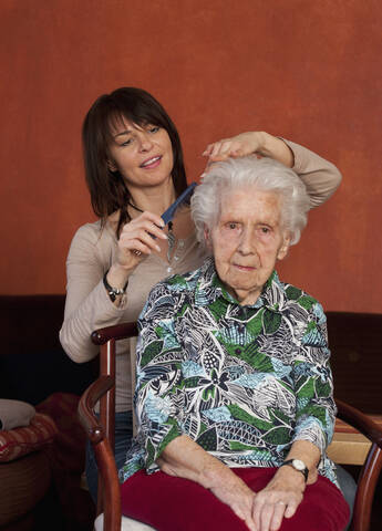 Ältere Frau kämmt die Haare einer älteren Frau, lächelnd, lizenzfreies Stockfoto