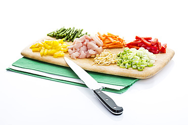 Karotten, grüne Bohnen, rohes Hühnerfleisch, Frühlingszwiebeln, Bohnensprossen und Paprika mit einem Messer auf einem Schneidebrett zerkleinern - MAEF005489