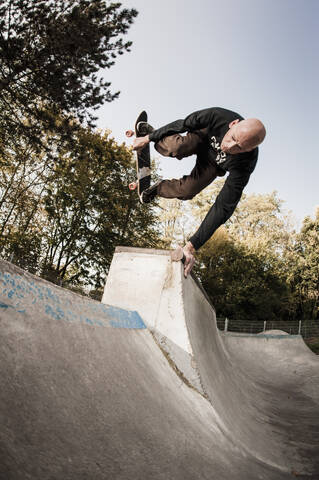Germany, North Rhine Westphalia, Duesseldorf, Mature man jumping with skateboard stock photo