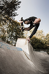 Germany, North Rhine Westphalia, Duesseldorf, Mature man jumping with skateboard - KJF000178