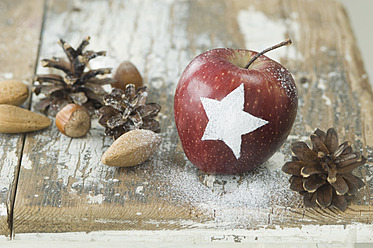 Weihnachtsapfel mit Schneestern, Tannenzapfen, Mandeln und Haselnüssen auf dem Tisch - ASF004755