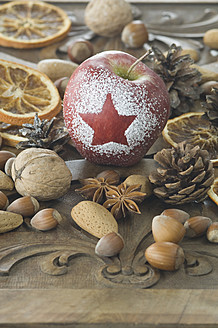 Weihnachtsapfel mit Schneestern, Haselnüssen, Walnüssen, Mandeln, Sternanis und Tannenzapfen auf dem Tisch - ASF004750