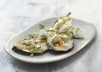 Plate of grilled aubergine with feta cheese on wooden table, close up - KSW001029