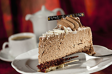 Scheibe Schokoladensahnetorte auf Teller, Kaffeegedeck im Hintergrund - CSF016192