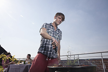 Deutschland, Berlin, Mann beim Grillen am Grill, lächelnd - RBF001168