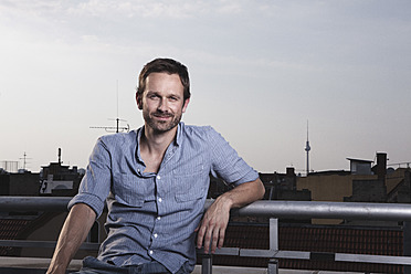 Germany, Berlin, Portrait of man on roof terrace, smiling - RBF001181