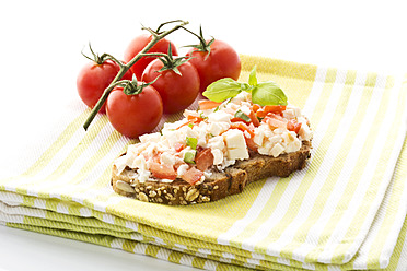 Mozzarella, tomatoes and basil on whole grain bread beside tomatoes, close up - MAEF005612