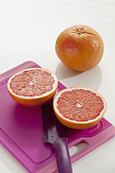 Grapefruit mit Schneidebrett und Messer auf weißem Hintergrund, Nahaufnahme - CSF016375