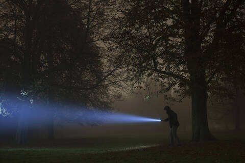 Deutschland, München, Junger Mann mit Taschenlampe in nebliger Nacht, lizenzfreies Stockfoto