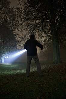 Deutschland, München, Junger Mann mit Taschenlampe in nebliger Nacht - FL000183