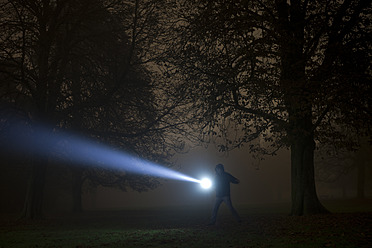 Germany, Munich, Man lighting spooky tree with torch in foggy night - FL000155