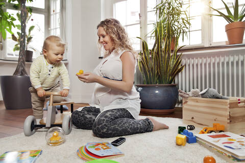 Deutschland, Bonn, Schwangere Mutter spielt mit Sohn im Wohnzimmer, lächelnd, lizenzfreies Stockfoto