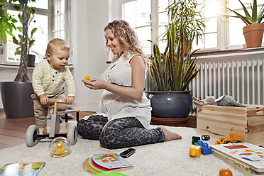 Deutschland, Bonn, Schwangere Mutter spielt mit Sohn im Wohnzimmer, lächelnd - MFF000517