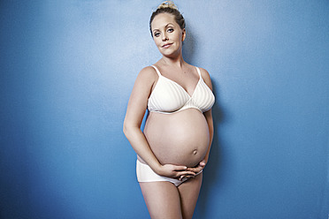 Schwangere Frau, die ihren Bauch hält, lächelnd, Porträt - MFF000495