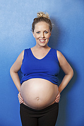 Schwangere Frau, die ihren Bauch hält, lächelnd, Porträt - MFF000497