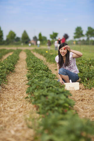 Deutschland, Bayern, Junge Japanerin zeigt Erdbeere im Feld, lizenzfreies Stockfoto