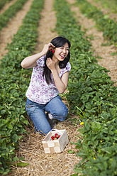 Germany, Bavaria, Young Japanese woman picking strawberries in field - FLF000204
