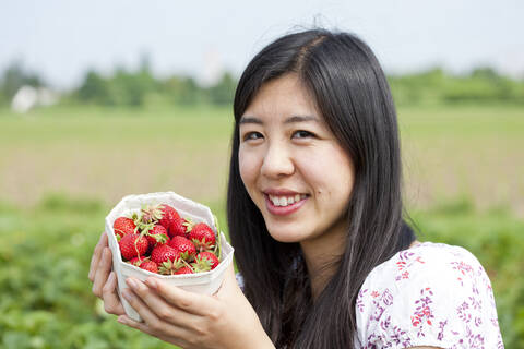 Deutschland, Bayern, Junge Japanerin pflückt Erdbeeren auf einem Feld, lizenzfreies Stockfoto