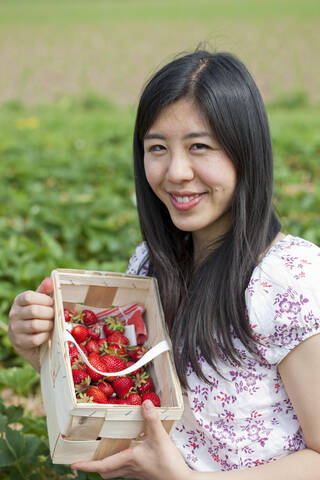 Deutschland, Bayern, Junge Japanerin pflückt Erdbeeren auf einem Feld, lizenzfreies Stockfoto