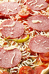 Pizza topped with salami, cheese and peppers on baking tray, close up - MAEF005673