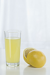 Glass of grapefruit juice beside grapefruit against white background, close up - ASF004777